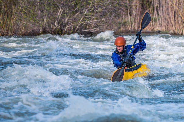 A kayaker struggling to paddle against the current, tipping over due to improper balance, and getting stuck in shallow waters