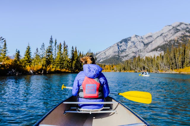 A sturdy kayak sits on a calm lake, surrounded by lush green trees and a clear blue sky. It shows signs of regular use but is well-maintained, with no visible damage